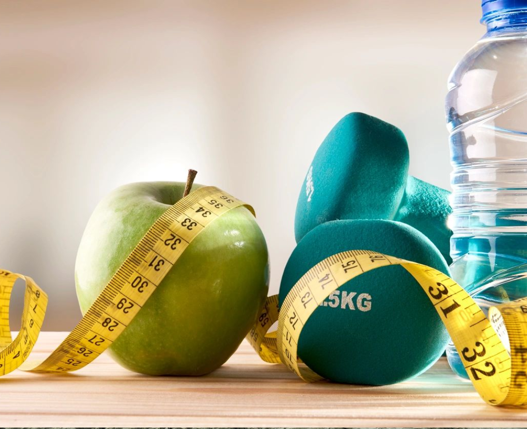 A green apple and measuring tape next to water bottle, dumbbell and water bottle.