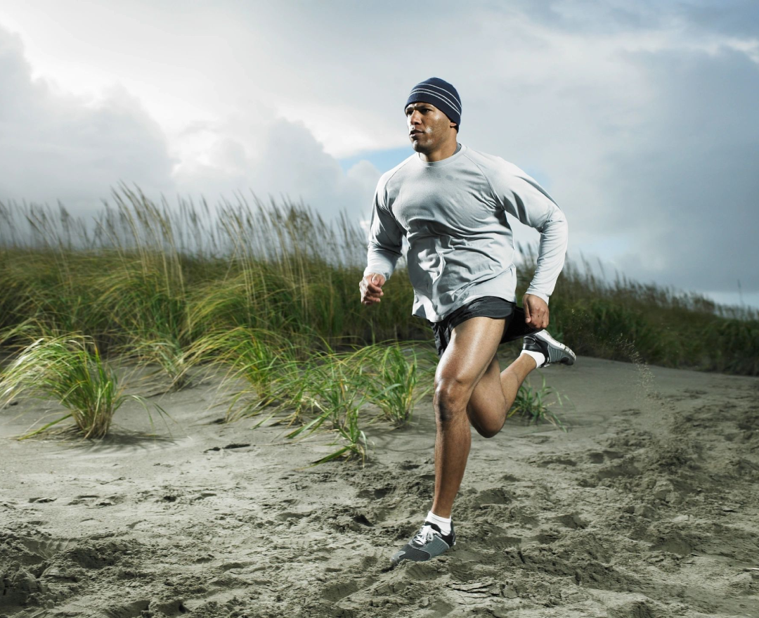 A man running on the beach in shorts.