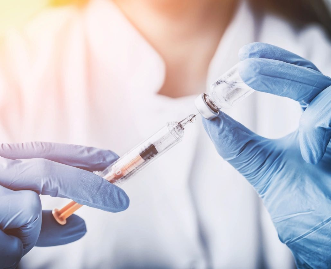 A person in blue gloves holding an injection.