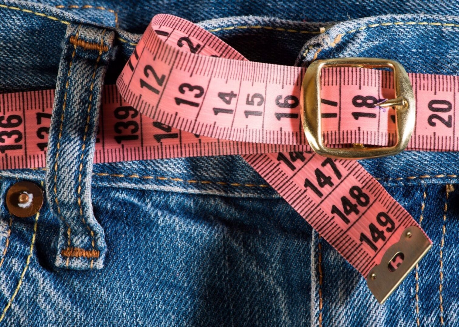 A pink measuring tape is wrapped around the waist of someone 's jeans.