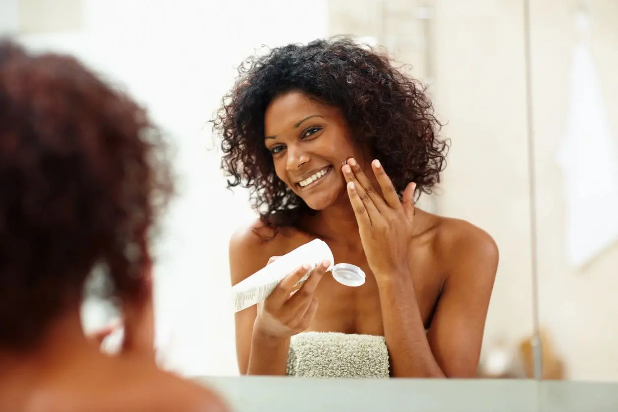 A woman is looking in the mirror and putting lotion on her face.